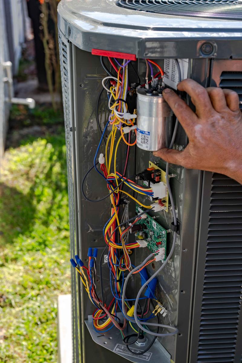 Air Conditioner Repair and Replacement 4 A Custom Air Conditioning Air Quality technician inspects the internal wiring and components of an outdoor air conditioning unit ensuring proper AC service and repair 2