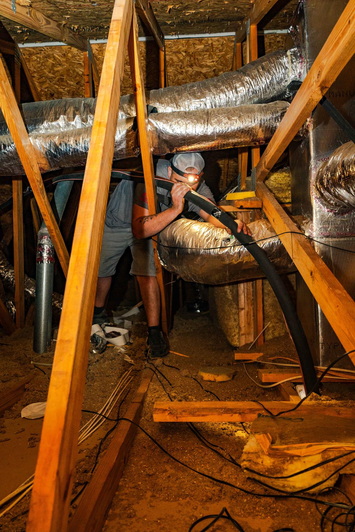 Ductwork 4 A technician in a tight attic space inspects and installs HVAC ductwork highlightinig the installation process for air conditioning systems by Custom Air Conditioning & Air Quality