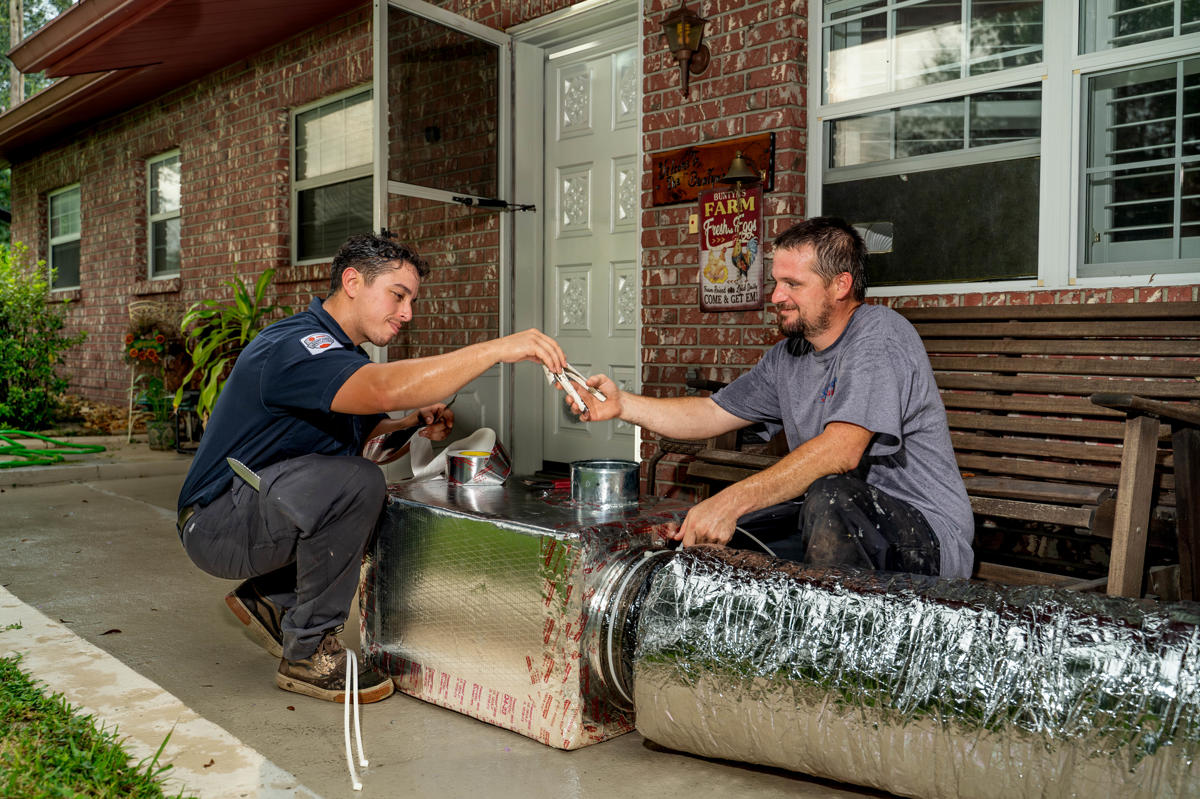 Ductwork 3 Two HVAC technicians work together outdoors on a large insulated air duct One technician hands a pair of pliers to the other as they collaborate on assembling ductwork